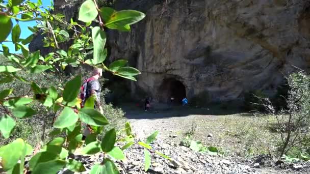 Guy Comes Large Cave Rock Follows Path Bushes Large Rock — Stock Video