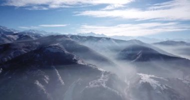 Dağların yamaçlarında sis yükseliyor. Yukarıdan, beyaz bulutlar, mavi gökyüzü ve kar tepeleri. Kış arazisi sisle kaplıydı. Hafif bir sis tabakası.