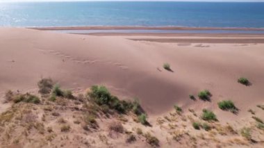 Okyanus kıyısında yüksek bir kum tepesi. Küçük sarı-yeşil otlar ve çalılar büyür. Suyun mavi rengi. Güneş ışıl ışıl parlıyor, suya yansıyor. İHA 'nın üst görüntüsü. Kapchagai
