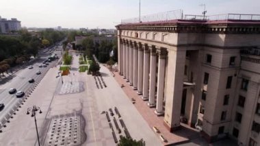 Almaty 'nin eski meydanının havadan görünüşü. Saraya benzeyen güzel bir bina. Çeşmelerin yanında, bir park ve bir yol. Kazak-İngiliz Teknik Üniversitesi 'nin çatısında Kazakistan bayrağı.