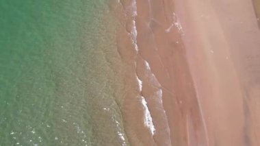 Deniz sarı kuma dalgalarla dokunuyor. Temiz bir sahil ve zümrüt sularındaki bir dronun üst görüntüsü. Güneş ışınları suya yansıtılır. Açık mavi gökyüzü. Rahatlamak için bir yer. Kapchagai