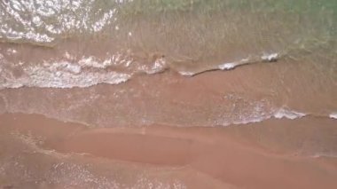 Deniz sarı kuma dalgalarla dokunuyor. Temiz bir sahil ve zümrüt sularındaki bir dronun üst görüntüsü. Güneş ışınları suya yansıtılır. Açık mavi gökyüzü. Rahatlamak için bir yer. Kapchagai