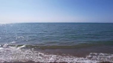 The sea touches the yellow sand with waves. Top view from a drone on a clean beach and emerald water. The suns rays are reflected in the water. Clear blue sky. A place for relaxation. Kapchagai