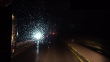 Otoyoldaki otobüs taksisinden görüntü. Pencereme yağmur damlaları yağıyor. Yol ıslak, arabalar bize doğru geliyor, farları parıldıyor. Yol işaretleri duruyor. Gece gezisi.