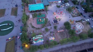 A birds-eye view of childrens attractions from a drone. Bright lights from different lanterns. Carousels are spinning. People are resting. The attractions are located on the shore of Lake Balkhash