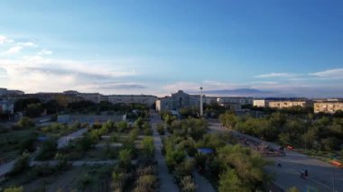 Aerial view from a drone of the small town of Balkhash on the shore of the lake. Low houses are painted in different colors, wide alleys, green trees grow. Cars are driving along the road. The clouds