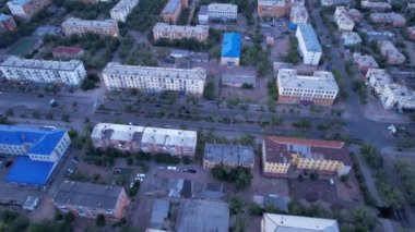 Aerial view from a drone of the small town of Balkhash on the shore of the lake. Low houses are painted in different colors, wide alleys, green trees grow. Cars are driving along the road. The clouds