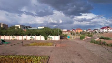Bright rainbow and rain over the city of Balkhash. The small town is all wet. Large clouds of white-blue color float by. Cars drive and people walk along the streets. Green trees are growing