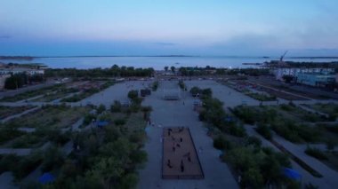 The embankment of the city of Balkhash. A ship is sailing on the lake. Dark green water, calm. Swifts fly. Bertys Bay. People walk along the beach and alleys. Blue clouds are visible in the distance