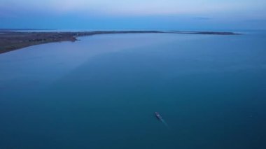 The embankment of the city of Balkhash. A ship is sailing on the lake. Dark green water, calm. Visible streaks of waves from the motor. Bertys Bay. People walk along the beach and alleys. Kazakhstan