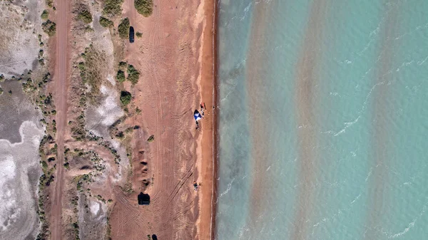 A beach with blue water color and sandy waves. Top view from a drone of vacationing people, tents and cars. Brown sand of Lake Balkhash. Bushes and several trees grow. Family vacation by sea