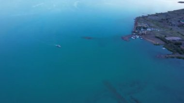 The embankment of the city of Balkhash. A ship is sailing on the lake. Dark green water, calm. Visible streaks of waves from the motor. Bertys Bay. People walk along the beach and alleys. Kazakhstan