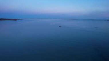 The embankment of the city of Balkhash. A ship is sailing on the lake. Dark green water, calm. Visible streaks of waves from the motor. Bertys Bay. People walk along the beach and alleys. Kazakhstan