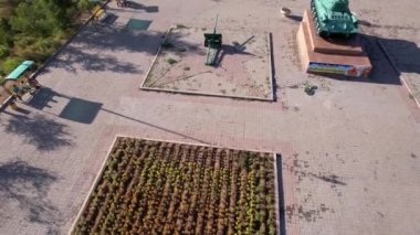 A real military tank on the shore of Lake Balkhash. There are two guns nearby. Monument about the Great Patriotic War of 1941 - 1945. Flowerbeds with flowers, an alley and green trees. Kazakhstan