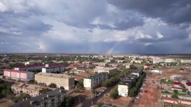 Bright rainbow and rain over the city of Balkhash. The small town is all wet. Large clouds of white-blue color float by. Cars drive and people walk along the streets. Green trees are growing