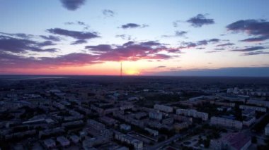 Pink sunset over a small town. Top view from a drone. The sun is sinking below the horizon. Blue-purple clouds on the background of houses and TV towers. Lights are on, cars are driving. Balkhash
