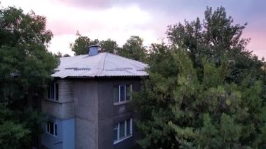 Beautiful sunset with big clouds over the city of Almaty. Aerial view from a drone of houses, cars and green trees. The sky shimmers with orange-purple color. The chimneys of factories are smoking
