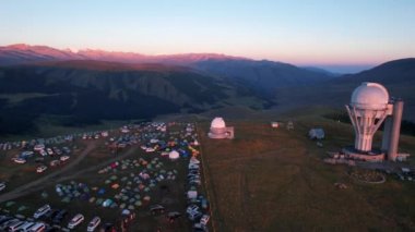 Bright dawn over the Assy-Turgen Observatory in the mountains. Aerial view from the drone of the camp of tents, cars and waking tourists. There is an old abandoned building. Kazakhstan, Almaty
