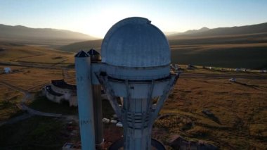 Bright dawn over the Assy-Turgen Observatory in the mountains. Aerial view from the drone of the camp of tents, cars and waking tourists. There is an old abandoned building. Kazakhstan, Almaty