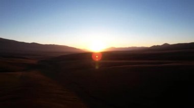 A bright yellow dawn with a red shade in the mountains. The green hills with grass turned red. A small stream runs through the gorge. Blue clear sky. Glare from the rays of the sun. Kazakhstan, Assy