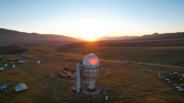 Bright dawn over the Assy-Turgen Observatory in the mountains. Aerial view from the drone of the camp of tents, cars and waking tourists. There is an old abandoned building. Kazakhstan, Almaty