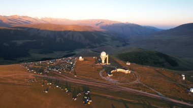 Bright dawn over the Assy-Turgen Observatory in the mountains. Aerial view from the drone of the camp of tents, cars and waking tourists. There is an old abandoned building. Kazakhstan, Almaty