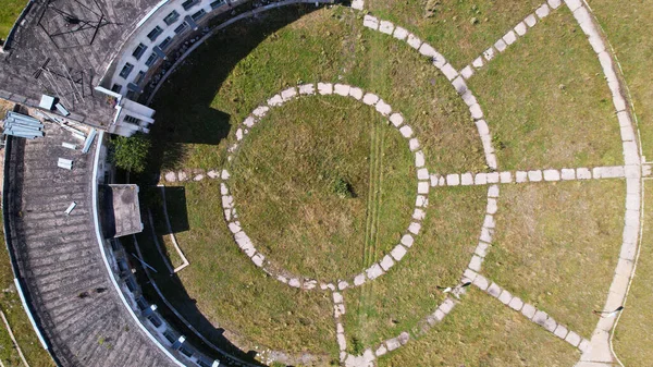 An abandoned building with a beautiful pattern of paths. The Assy-Turgen Observatory. The paths are laid out in the form of a telescope. Green grass grows, and purple bushes grow on the roof. Drone