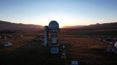 Bright dawn over the Assy-Turgen Observatory in the mountains. Aerial view from the drone of the camp of tents, cars and waking tourists. There is an old abandoned building. Kazakhstan, Almaty