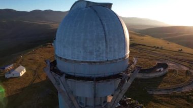 Bright dawn over the Assy-Turgen Observatory in the mountains. Aerial view from the drone of the camp of tents, cars and waking tourists. There is an old abandoned building. Kazakhstan, Almaty