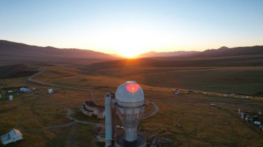 Bright dawn over the Assy-Turgen Observatory in the mountains. Aerial view from the drone of the camp of tents, cars and waking tourists. There is an old abandoned building. Kazakhstan, Almaty