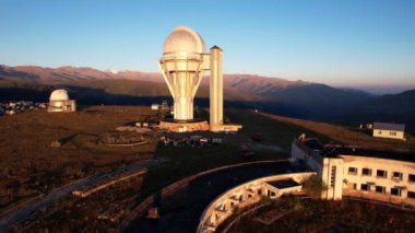 Bright dawn over the Assy-Turgen Observatory in the mountains. Aerial view from the drone of the camp of tents, cars and waking tourists. There is an old abandoned building. Kazakhstan, Almaty