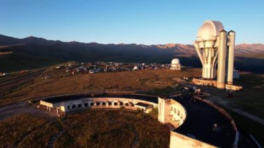 Bright dawn over the Assy-Turgen Observatory in the mountains. Aerial view from the drone of the camp of tents, cars and waking tourists. There is an old abandoned building. Kazakhstan, Almaty