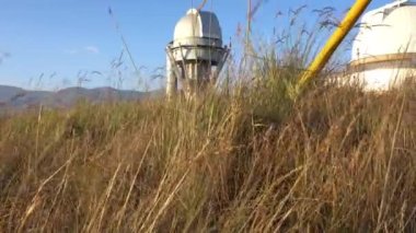 Large buildings of the observatory in the form of a dome. The telescopes are closed. Beautiful tall yellow-green grass develops in the wind. Blue sky and green hills in the distance. The Assy Plateau