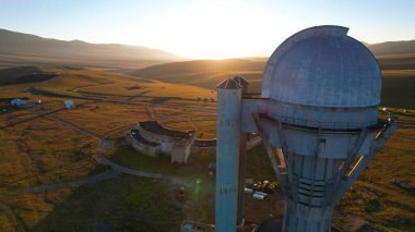 Bright dawn over the Assy-Turgen Observatory in the mountains. Aerial view from the drone of the camp of tents, cars and waking tourists. There is an old abandoned building. Kazakhstan, Almaty