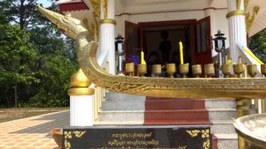 Tayland 'daki Budist tapınağı. Küçük ahşap bir gemi. Lezzetli çubuklar var. Arka planda, tapınağın girişi. Yaldızlı kolonlar ve basamaklar. Yeşil ağaçlar büyür.