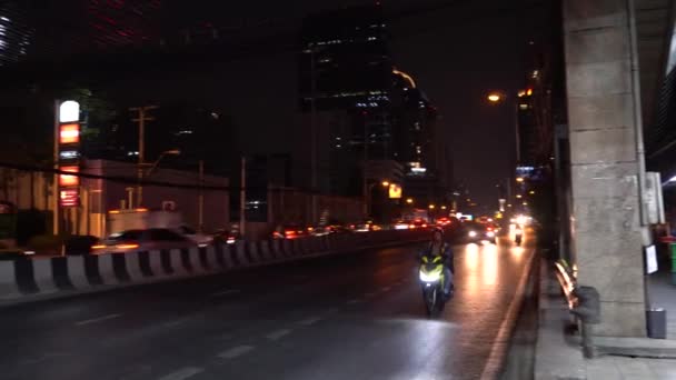 バンコクの夜の街 道路上の車の多く どこかに渋滞があった オートバイの人々はすぐに渡します すべてが成長する 歩道はほとんど空です 看板が点いてる — ストック動画