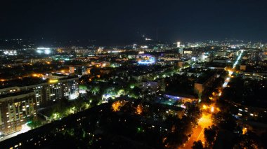 Almaty 'nin gece şehrinin yüksekliğinden bak. Farklı ışıklar ışıl ışıl parlıyor. Arabalar yollarda gidiyor. Kok-Tobe TV kulesi uzaktan görülebiliyor. Pencerelerde ışıklar yanıyor.