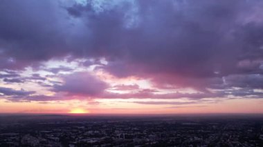 Epic yellow-pink-blue sunset over the city of Almaty. Large dark blue clouds shimmer with different colors. The sun goes below the horizon. Cars drive along the road, trees grow among low houses