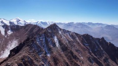 Karlı kayalık dağ tepeleri açık bir sis bulutu içinde. Mavi gökyüzünün insansız hava aracı, açık sis ve dik tepeli uçurumlar. Uzaktan bir moraine gölü görülebilir. Eski buzullar. Kazakistan
