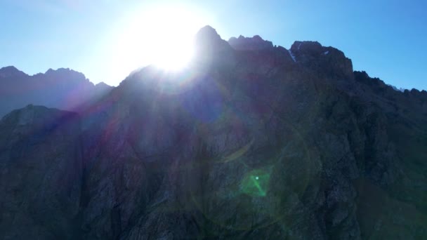 太阳从陡峭的悬崖后面出来了 明亮的光线会产生眩光和阴影 在高山上 有些地方有绿色的灌木丛和黄色的草 秋天在山上 蓝天无人机视图 — 图库视频影像