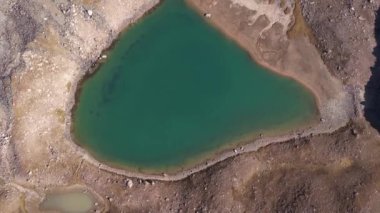 Bir dağ gölünün sularının zümrüt rengi. Dağların yansıması olan yeşil bir dağ gölünün drone görüntüsü. Pürüzsüz şeffaf su. Yakınlarda büyük taşlar var. Kuru çimler Kazakistan