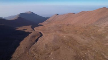 Sonbahar dağları. Nehir vadide kurudu. İHA 'nın sarı çimlerdeki ve bazen de yeşil çalılardaki görüntüsü. Nehir yatağı neredeyse kurudu. Gri duman uzaktan görülebilir. Kazakistan