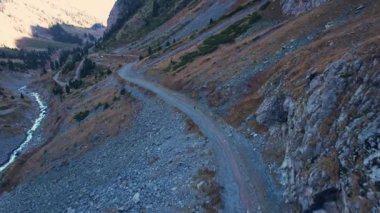Adam vadi boyunca dağlarda yürüyor. Dik bir uçurumu ve nehri olan yüksek dağlar. Vadi boyunca toprak bir yol var. Yeşil çalılar ve şimdiden sarı otlar yetişti.