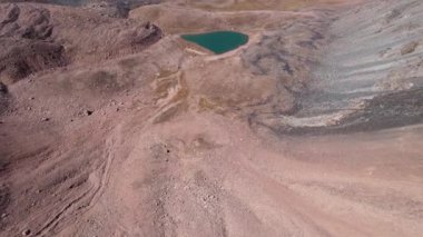 Bir dağ gölünün sularının zümrüt rengi. Dağların yansıması olan yeşil bir dağ gölünün drone görüntüsü. Pürüzsüz şeffaf su. Yakınlarda büyük taşlar var. Kuru çimler Kazakistan