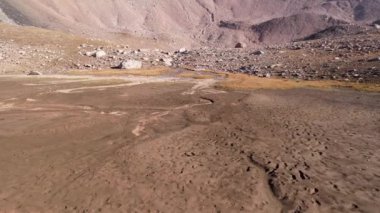 Dağlardaki kurumuş bir nehir yatağının drone görüntüsü. Islak kumda ayakkabı izleri. Sarı çimenler ve büyük kayalar. Bir dağ geçidine çıkan dik bir vadi. Kazakistan. Trans Dağları - Ili Alatau