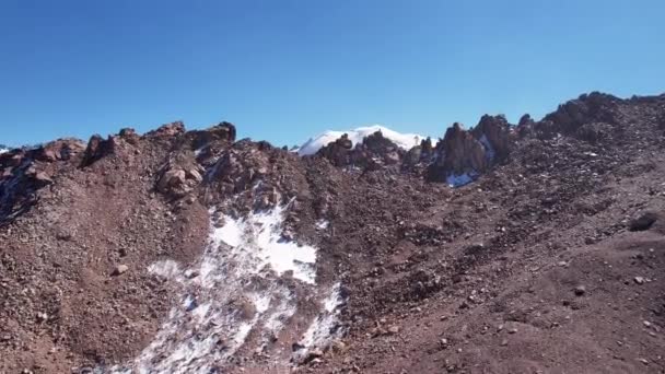 雪の山を見下ろす岩のパス 急な崖や大きな岩 青い澄んだ空 山の峰々は雪に覆われている 無人機からの眺め 緩やかな石の痕跡 カザフスタン — ストック動画