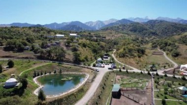 Dağlarda otelleri olan bir çiftliğin insansız hava aracı görüntüsü. Güzel büyük gölet, yeşil tepeler ve uzun ağaçlar. Birkaç otel var, oteller var. Arabalar için yol ve park yeri. Aileyle bir hafta sonu için bir fazenda.