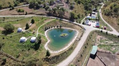 Dağlarda otelleri olan bir çiftliğin insansız hava aracı görüntüsü. Güzel büyük gölet, yeşil tepeler ve uzun ağaçlar. Birkaç otel var, oteller var. Arabalar için yol ve park yeri. Aileyle bir hafta sonu için bir fazenda.