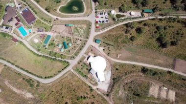 Dağlarda otelleri olan bir çiftliğin insansız hava aracı görüntüsü. Güzel büyük gölet, yeşil tepeler ve uzun ağaçlar. Birkaç otel var, oteller var. Arabalar için yol ve park yeri. Aileyle bir hafta sonu için bir fazenda.