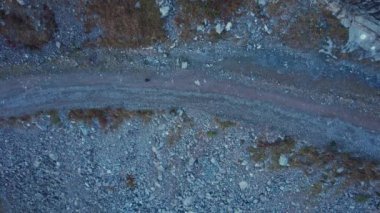 Adam vadi boyunca dağlarda yürüyor. Dik bir uçurumu ve nehri olan yüksek dağlar. Vadi boyunca toprak bir yol var. Yeşil çalılar ve şimdiden sarı otlar yetişti.